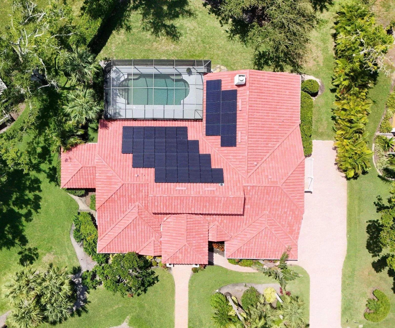 Top-down drone view of solar panels arranged across a red tile roof beside a screened pool