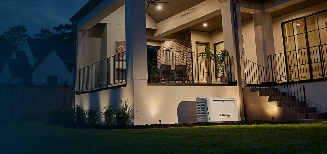 Generac standby generator beside the stairs of a home at night, running while the porch lights stay on