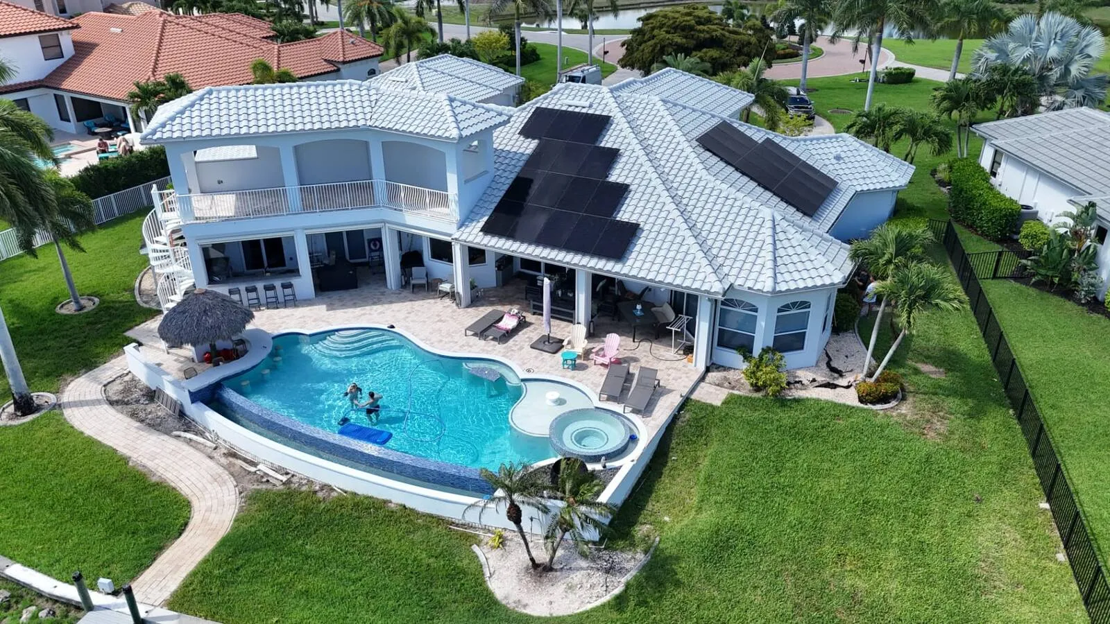 Aerial view of a Florida tile roof with two arrays of solar panels beside a swimming pool, installed by Coastal Energy