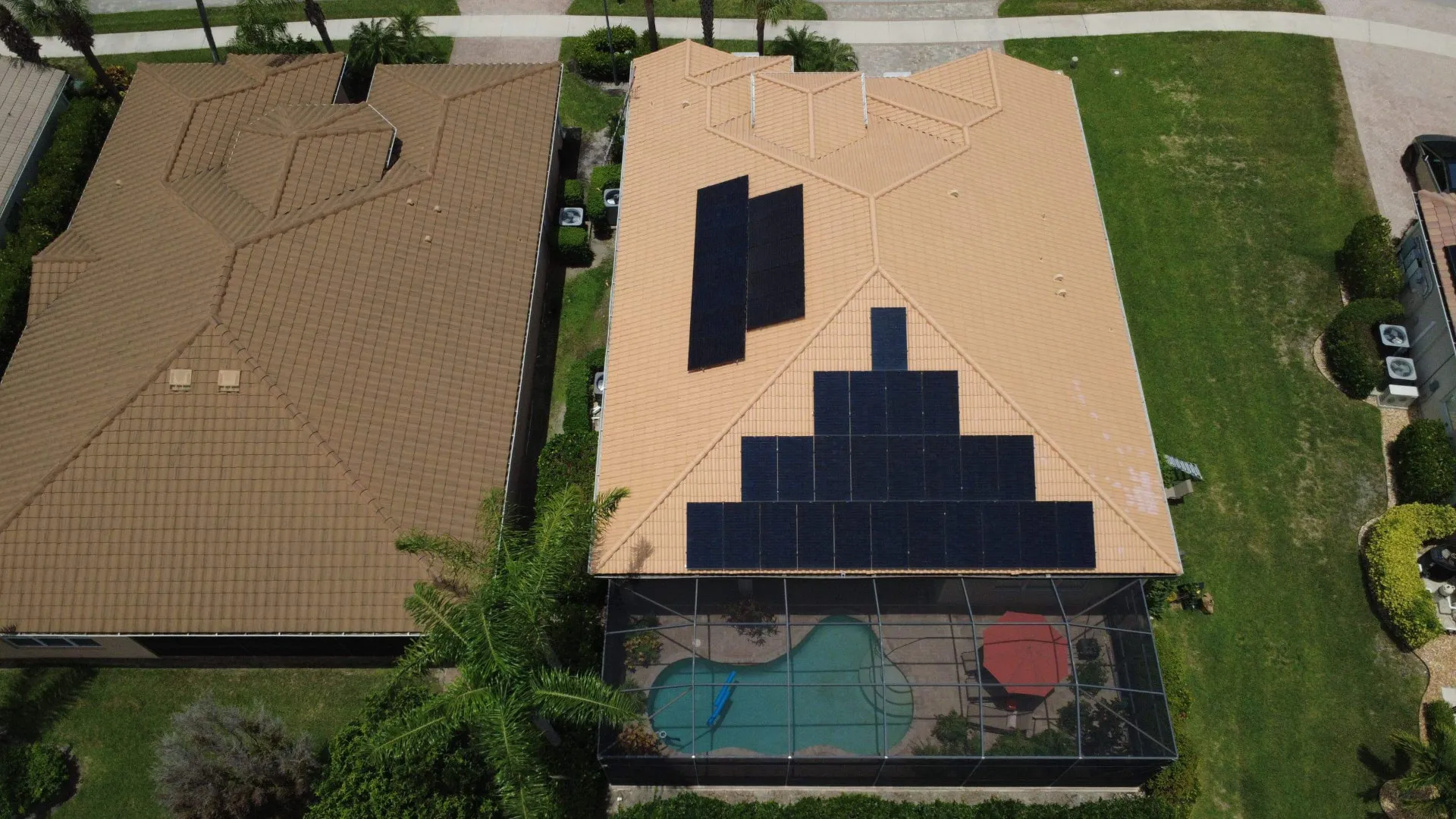 Top down aerial of a black solar array on a barrel tile roof over a pool cage home in Bonita Springs, Florida